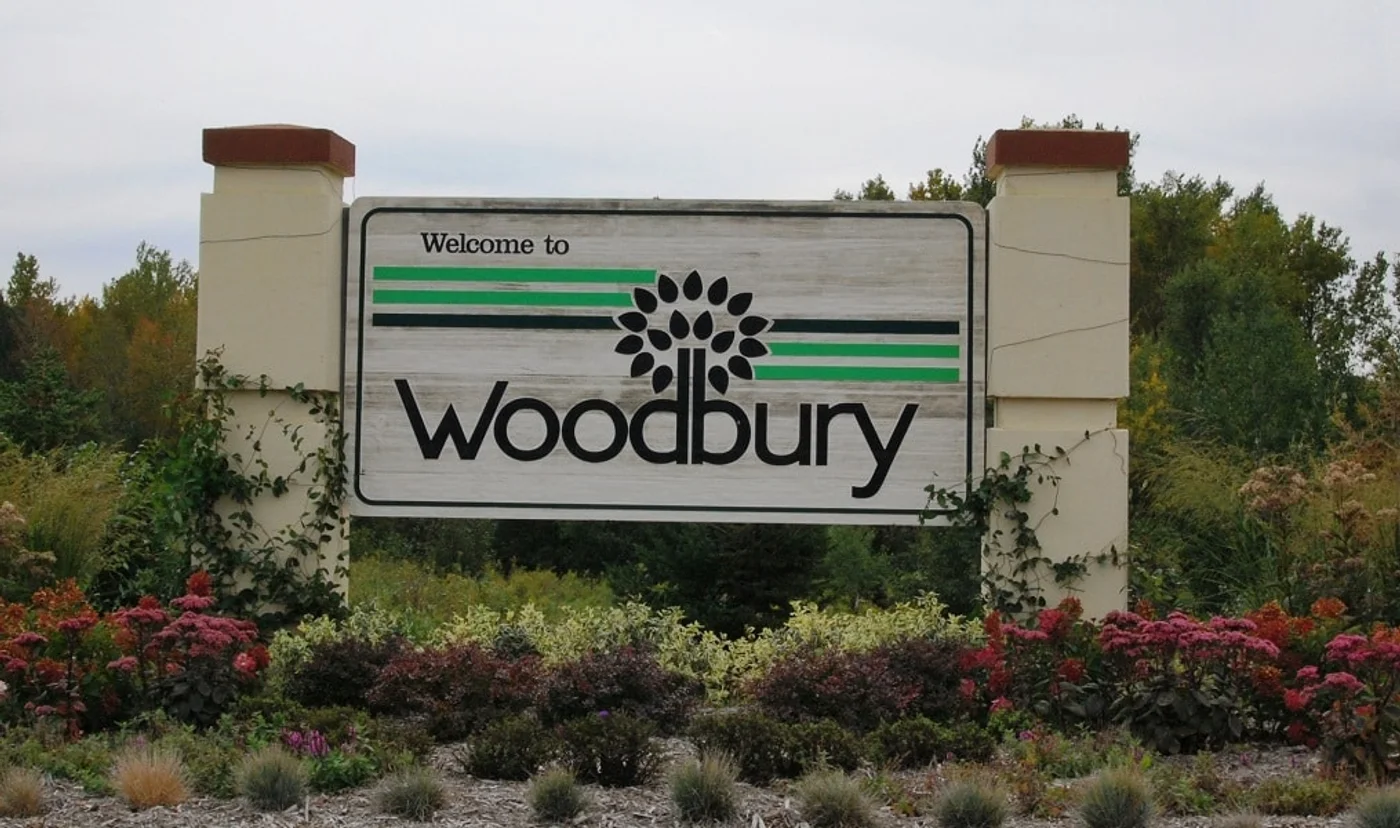 The Welcome to Woodbury sign, surrounded by flowers and trees
